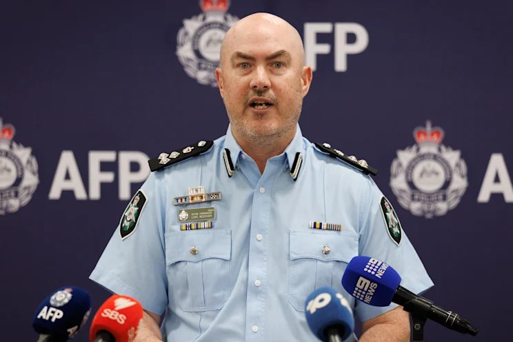 AFP Acting Commander Luke Needham speaking at a press conference in front of AFP crests, with broadcast microphones in front of him