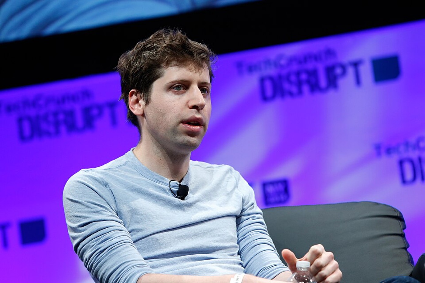 A young Sam Altman on stage at a technology conference, seated and speaking